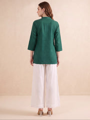 A woman is shown from the back wearing a dark green three-quarter sleeve kurta paired with white wide-leg trousers, standing against a neutral beige background.