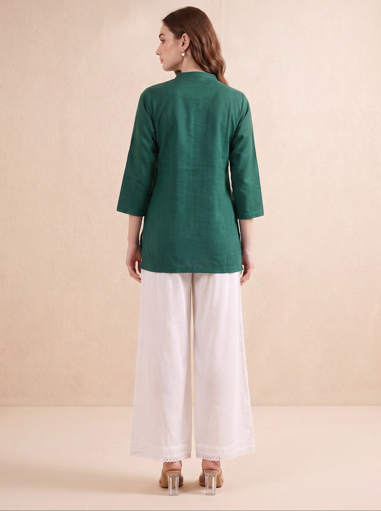 A woman is shown from the back wearing a dark green three-quarter sleeve kurta paired with white wide-leg trousers, standing against a neutral beige background.