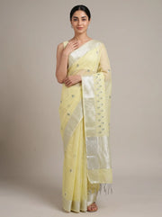 A woman modeling a pale yellow saree with a wide silver border and small embroidered motifs, standing against a plain beige studio background.
