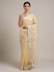 A woman modeling a pale yellow semi-sheer saree with pink floral embroidery and a silver-toned striped border, photographed against a plain beige studio background.