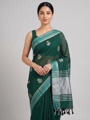 A woman modeling a dark green saree with a silver border, silver floral motifs, and black tassels, set against a plain light gray background.