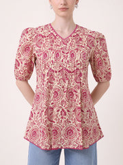 A woman wearing a short-sleeve V-neck kurti top with a pink and beige circular floral pattern, paired with blue jeans, shown against a plain light background.