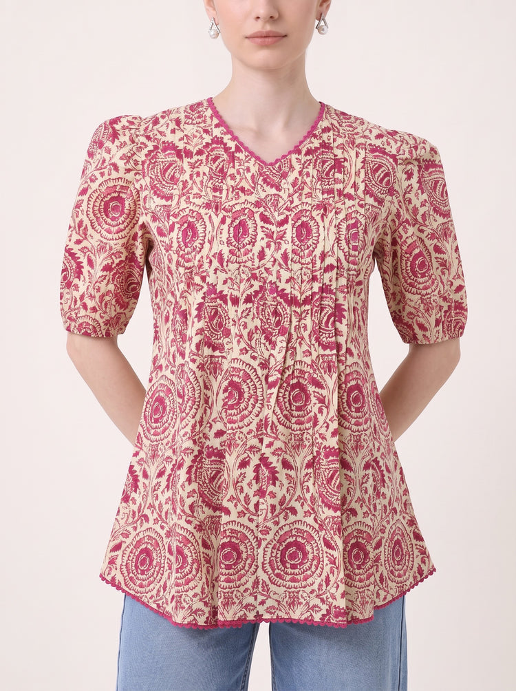 A woman wearing a short-sleeve V-neck kurti top with a pink and beige circular floral pattern, paired with blue jeans, shown against a plain light background.