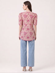 A woman shown from the back wearing a pink and beige paisley printed short-sleeve kurti with light blue jeans and metallic heels, against a plain light beige studio background.