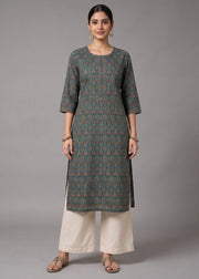 A woman modeling a dark gray-green printed kurta with orange and blue geometric patterns, paired with cream-colored wide-leg pants, against a solid gray studio background.