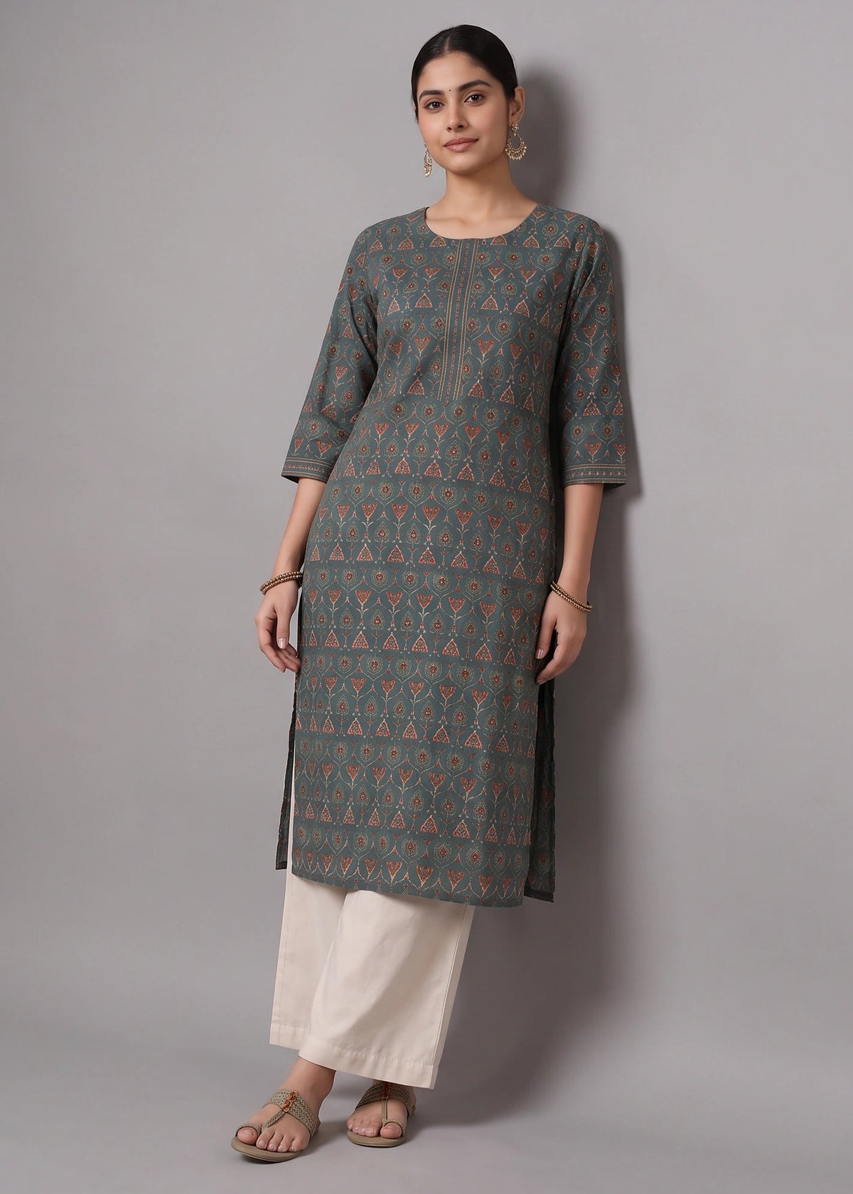 A woman modeling a three-quarter sleeve kurta with a gray base and orange geometric print, paired with off-white pants, against a solid gray studio background.