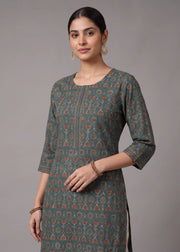 A woman modeling a three-quarter sleeve kurta in a muted teal-green color with a repeating orange and beige geometric block print pattern, set against a plain gray studio background.