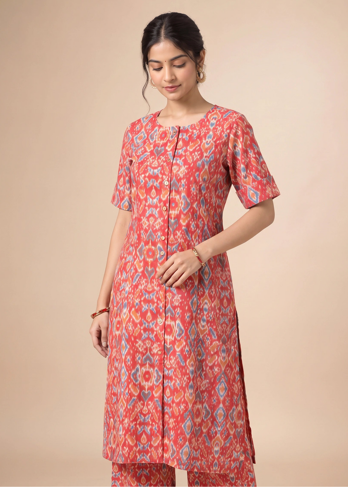 A woman modeling a coral pink kurta with a blue and yellow ikat pattern, paired with matching pants, against a solid beige background.