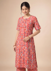 A woman modeling a coral pink kurta with a blue and yellow ikat pattern, paired with matching pants, against a solid beige background.