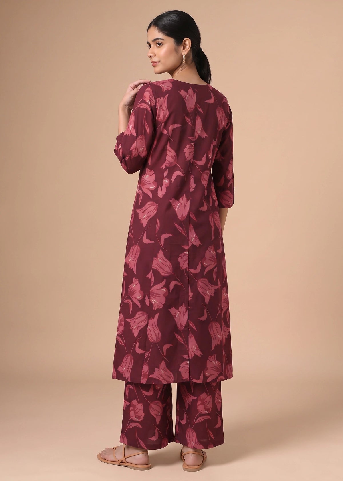 A woman modeling a three-piece maroon floral kurta set, shown from the back against a solid beige studio background.