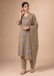 A woman modeling a traditional Indian salwar kameez suit set in a warm beige color, featuring a printed kurta with blue circular motifs and a matching dupatta, set against a solid beige studio background.