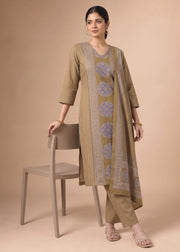 A woman models a beige and light blue printed kurta set with matching pants, standing next to a matching beige chair against a solid beige background.