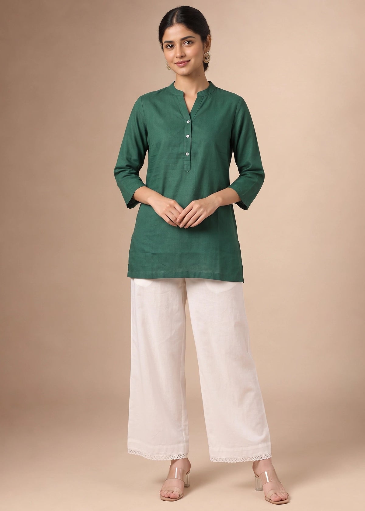 A woman modeling a dark green three-quarter sleeve kurta with a buttoned neckline, paired with off-white wide-leg trousers, against a solid beige studio background.