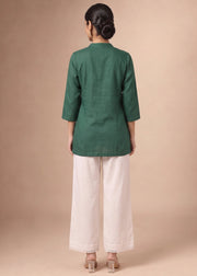 A woman viewed from the back wearing a dark green three-quarter sleeve kurta and off-white wide-leg trousers, standing against a solid beige studio background.