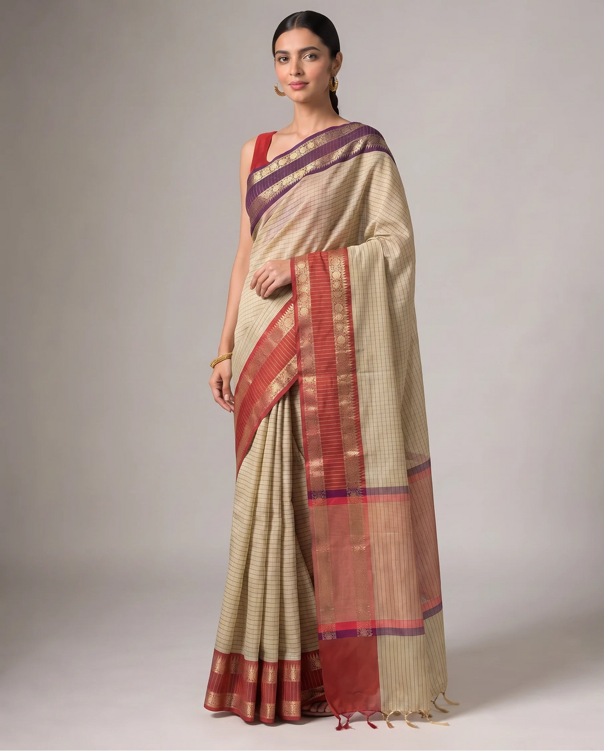 A woman models a traditional Indian saree with a beige body, a deep purple border, and a rust-red and gold zari woven border, set against a plain light gray studio background.