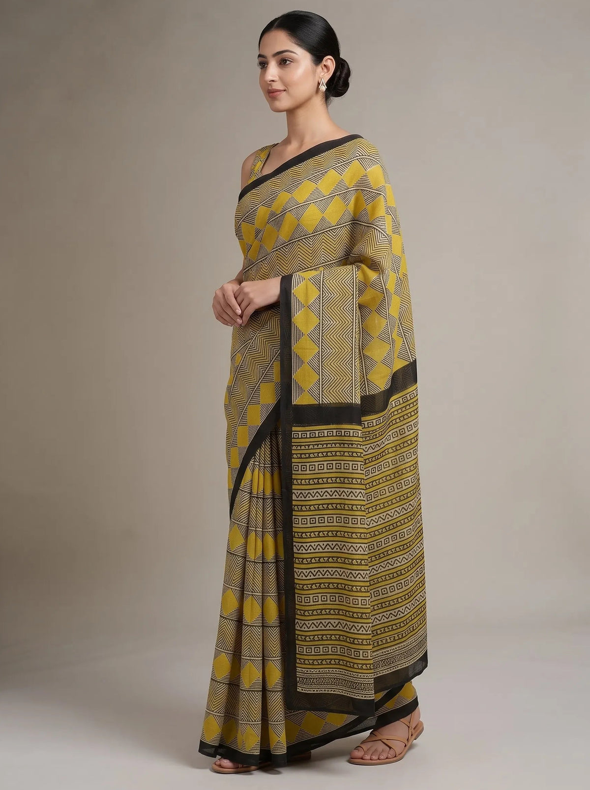 A woman modeling a mustard yellow and black patterned cotton saree against a neutral beige studio background.