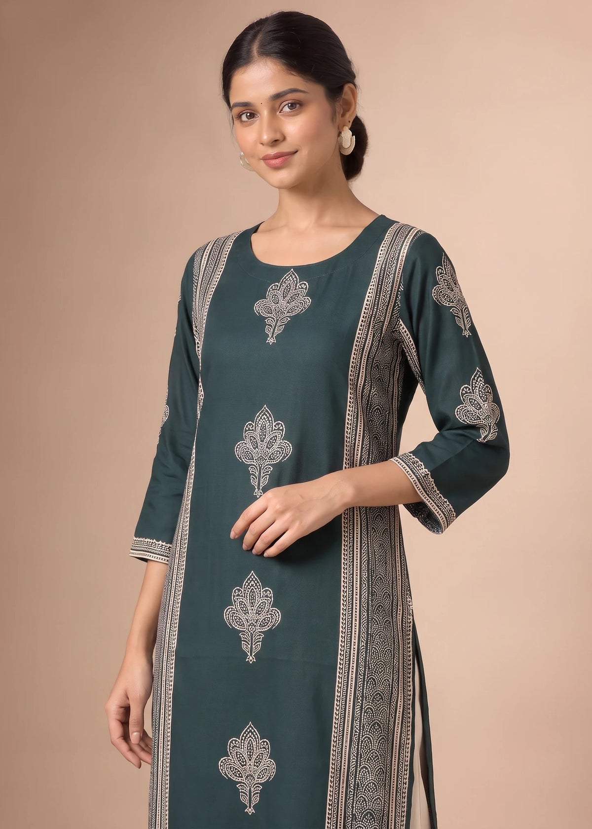 A woman modeling a dark teal green kurta with silver-gray printed motifs and borders, set against a solid beige background.