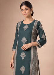 A woman modeling a dark teal green kurta with silver-gray printed motifs and borders, set against a solid beige background.