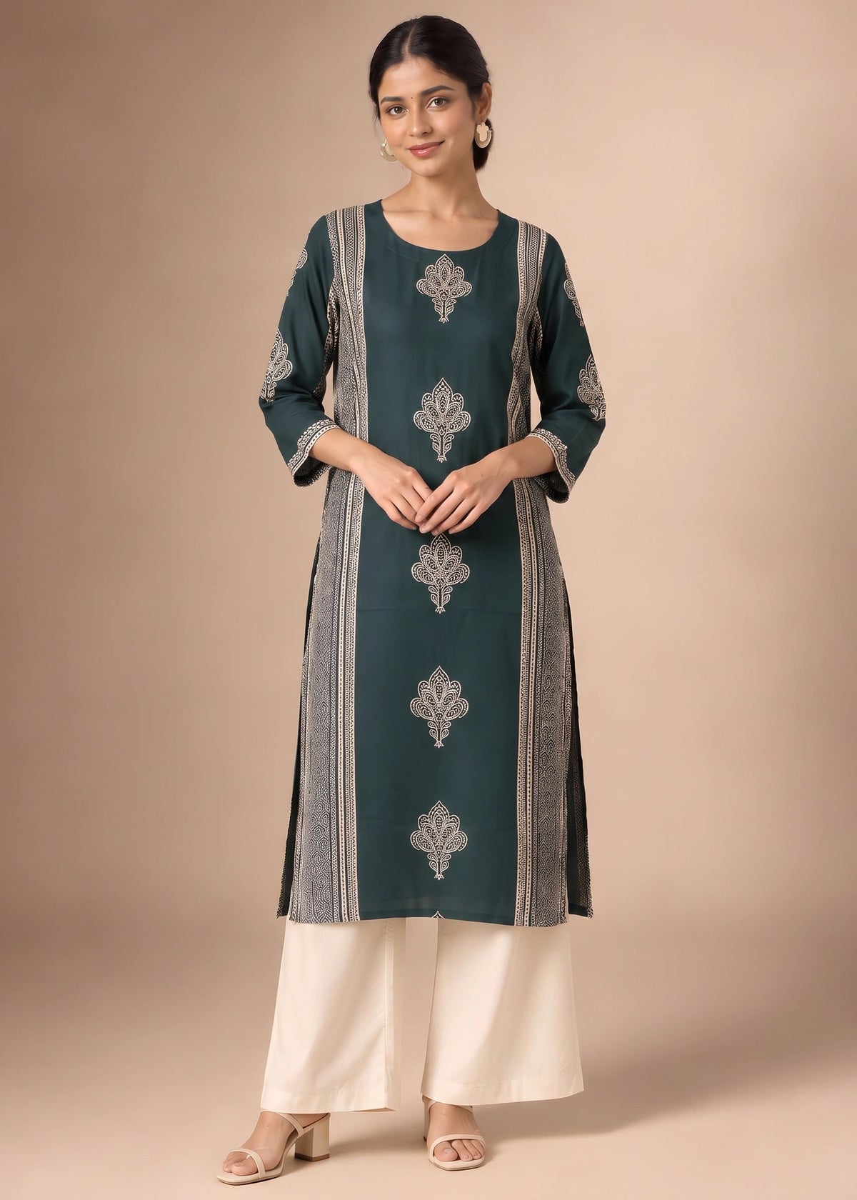 A woman modeling a dark teal green kurta with silver-gray printed motifs and vertical stripes, paired with off-white wide-leg pants, against a solid beige studio background.