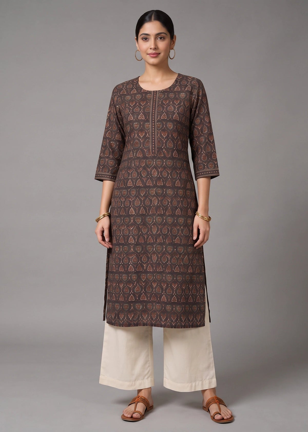 A woman modeling a brown printed kurta with three-quarter sleeves, paired with off-white wide-leg pants and brown sandals, against a solid gray studio background.