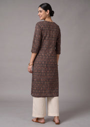 A woman stands with her back to the camera wearing a brown patterned kurta with three-quarter sleeves and cream-colored cropped pants, set against a plain gray studio background.