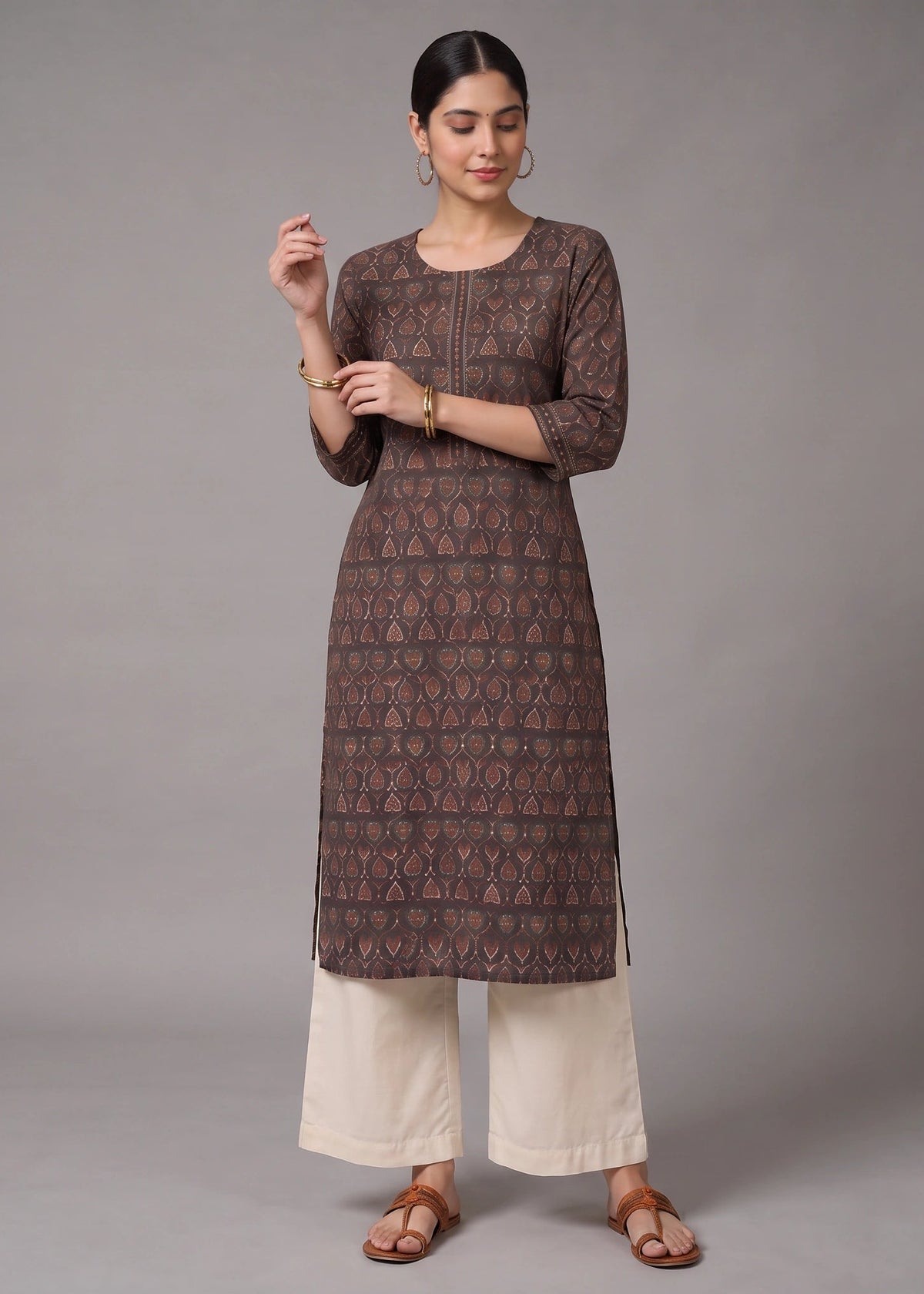 A woman modeling a brown printed kurta with three-quarter sleeves, paired with off-white wide-leg pants and brown sandals, against a solid gray studio background.