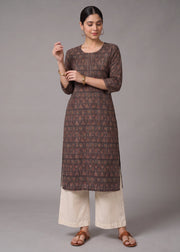 A woman modeling a brown printed kurta with three-quarter sleeves, paired with off-white wide-leg pants and brown sandals, against a solid gray studio background.