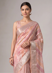 A woman modeling a coral orange and pink saree with metallic silver stripes and a silver border, set against a plain gray studio background.