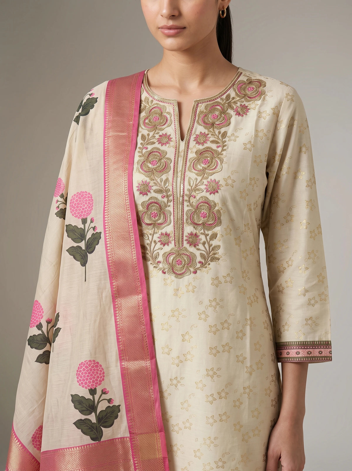 A woman wearing a cream-colored embroidered kurta with pink floral embroidery and a matching pink dupatta with floral motifs, shown against a neutral gray background.