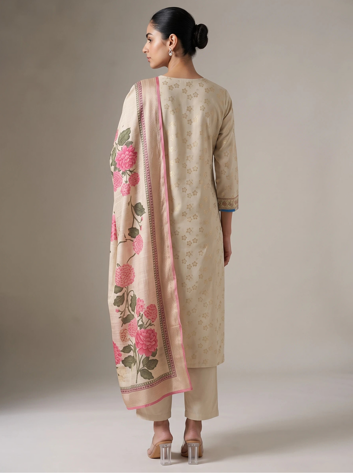 A woman shown from the back wearing a beige traditional outfit with a matching dupatta featuring pink floral embroidery and a pink border, against a plain studio background.