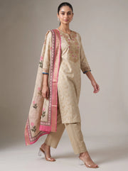 A woman models a traditional beige salwar kameez suit with pink border accents and floral embroidery, paired with matching beige trousers and a pink dupatta, against a neutral studio background.