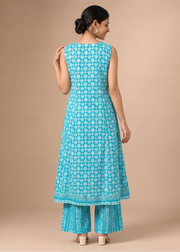 A woman shown from the back wearing a turquoise blue printed kurta and matching palazzo pants against a solid beige studio background.
