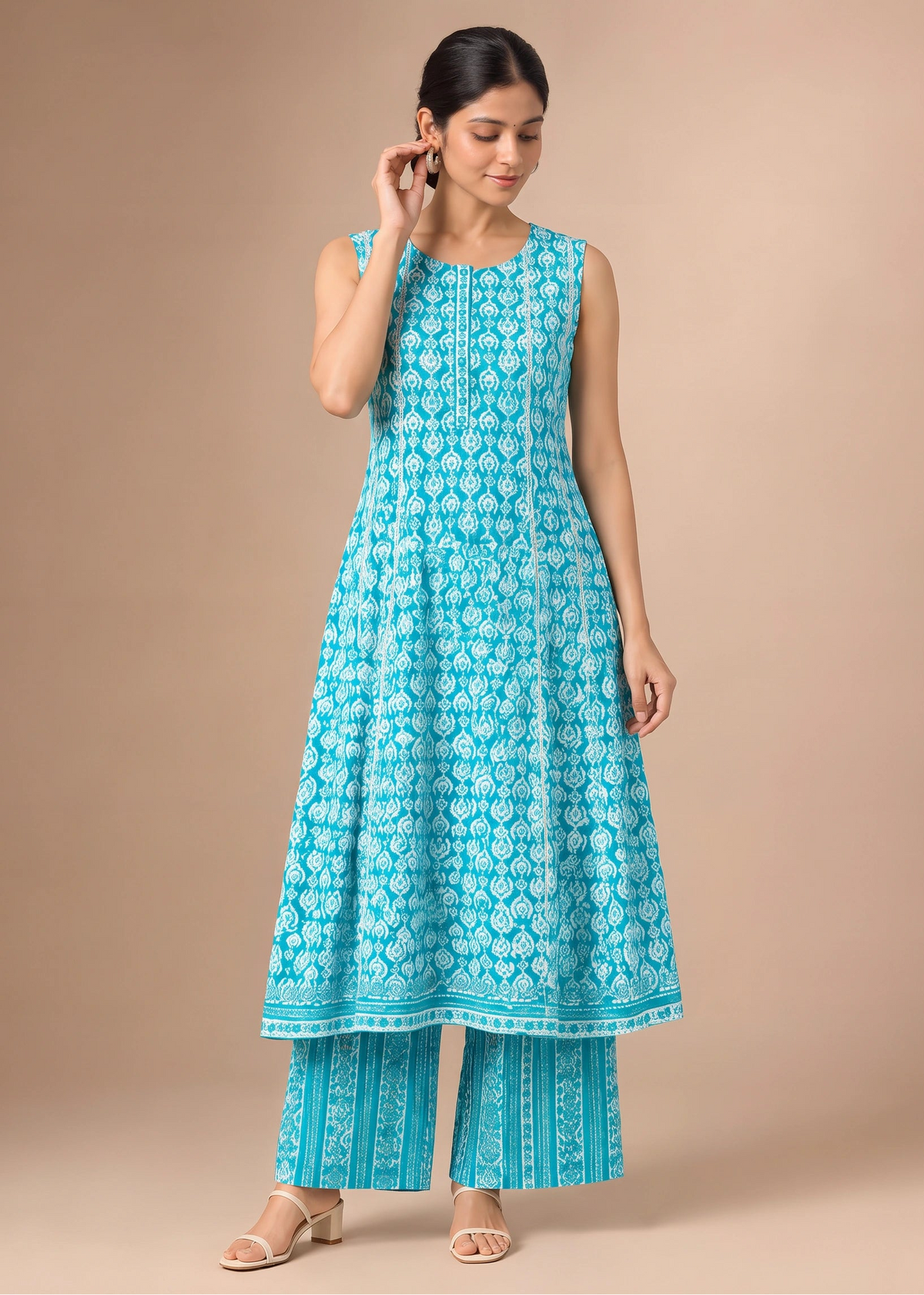 A woman modeling a sleeveless turquoise blue and white printed kurta with matching wide-leg pants, standing against a solid beige studio background.