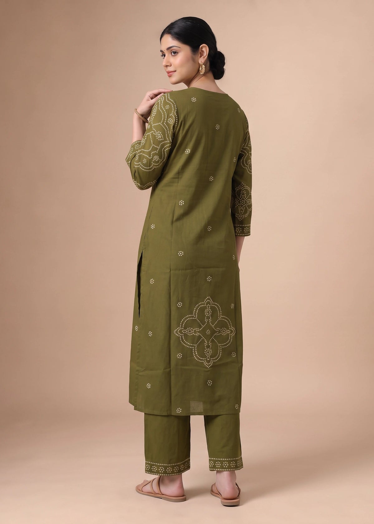 A woman modeling an olive green kurta set with beige embroidery, shown from the back against a solid beige studio background.