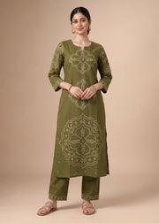 A woman modeling an olive green kurta set with beige geometric and floral embroidery, paired with matching pants, against a solid beige studio background.