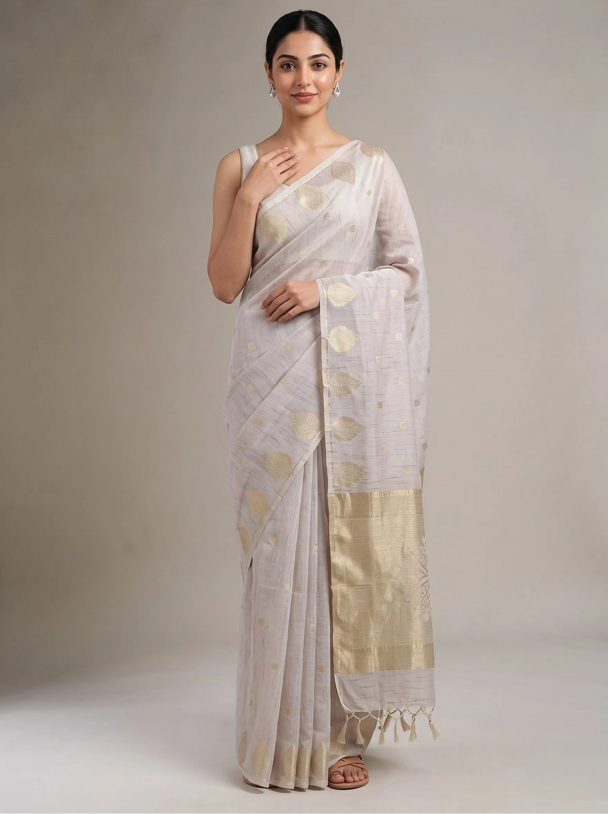 A woman modeling a lilac purple saree with gold zari motifs and a wide gold border, standing against a neutral beige studio backdrop.