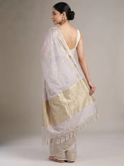 A woman modeling a lilac purple saree from the back, showing the gold foil motifs, border, and tassel fringe against a neutral studio background.