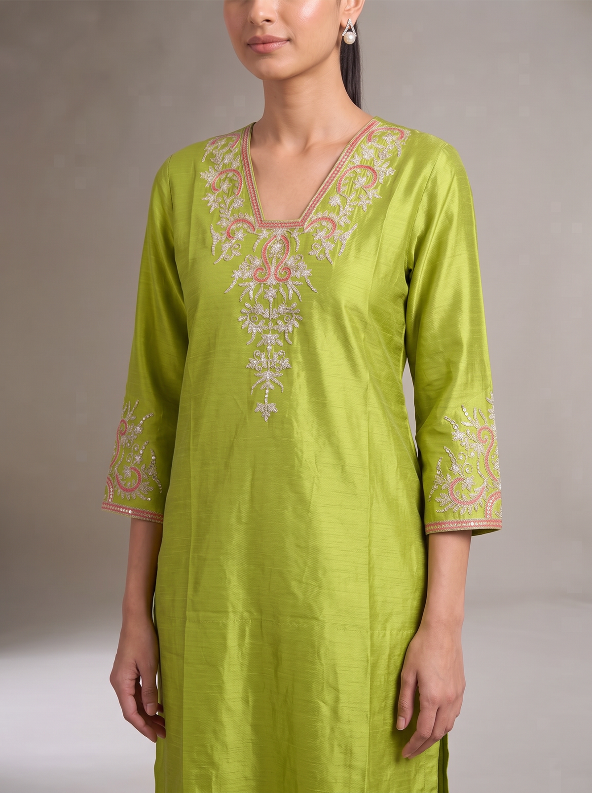 A woman wearing a lime green kurta with white and pink floral embroidery around the V-neck and sleeve cuffs, photographed against a neutral gray studio background.