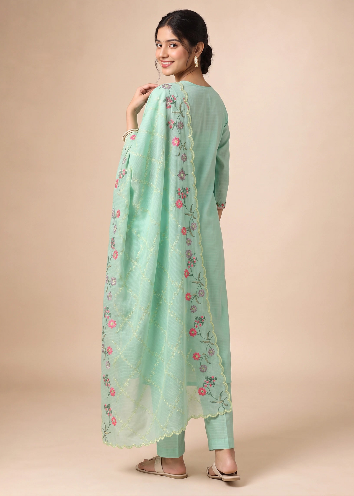 A woman modeling a mint green traditional outfit with a matching embroidered dupatta, photographed against a solid beige studio background.