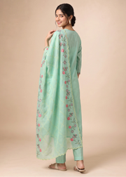 A woman modeling a mint green traditional outfit with a matching embroidered dupatta, photographed against a solid beige studio background.