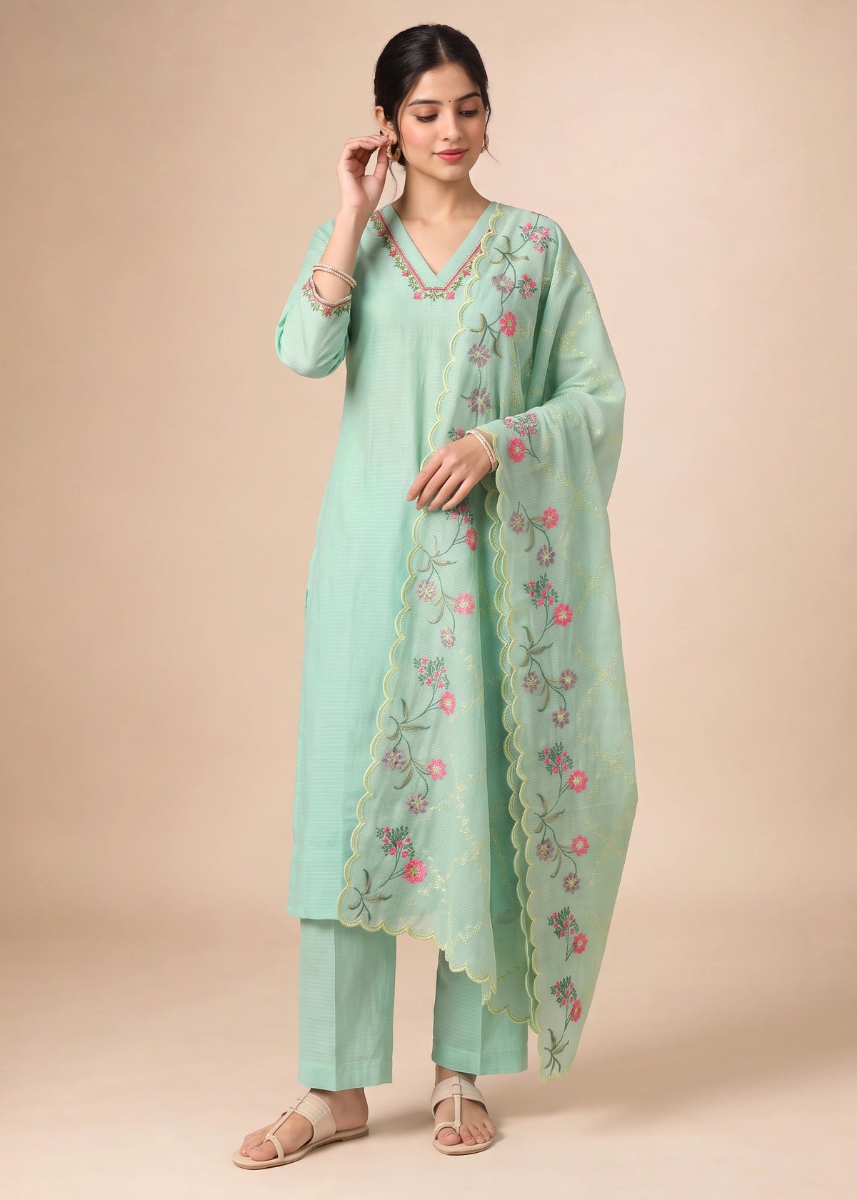 A woman modeling a mint green traditional Indian salwar kameez suit with matching embroidered dupatta, set against a solid beige studio background.