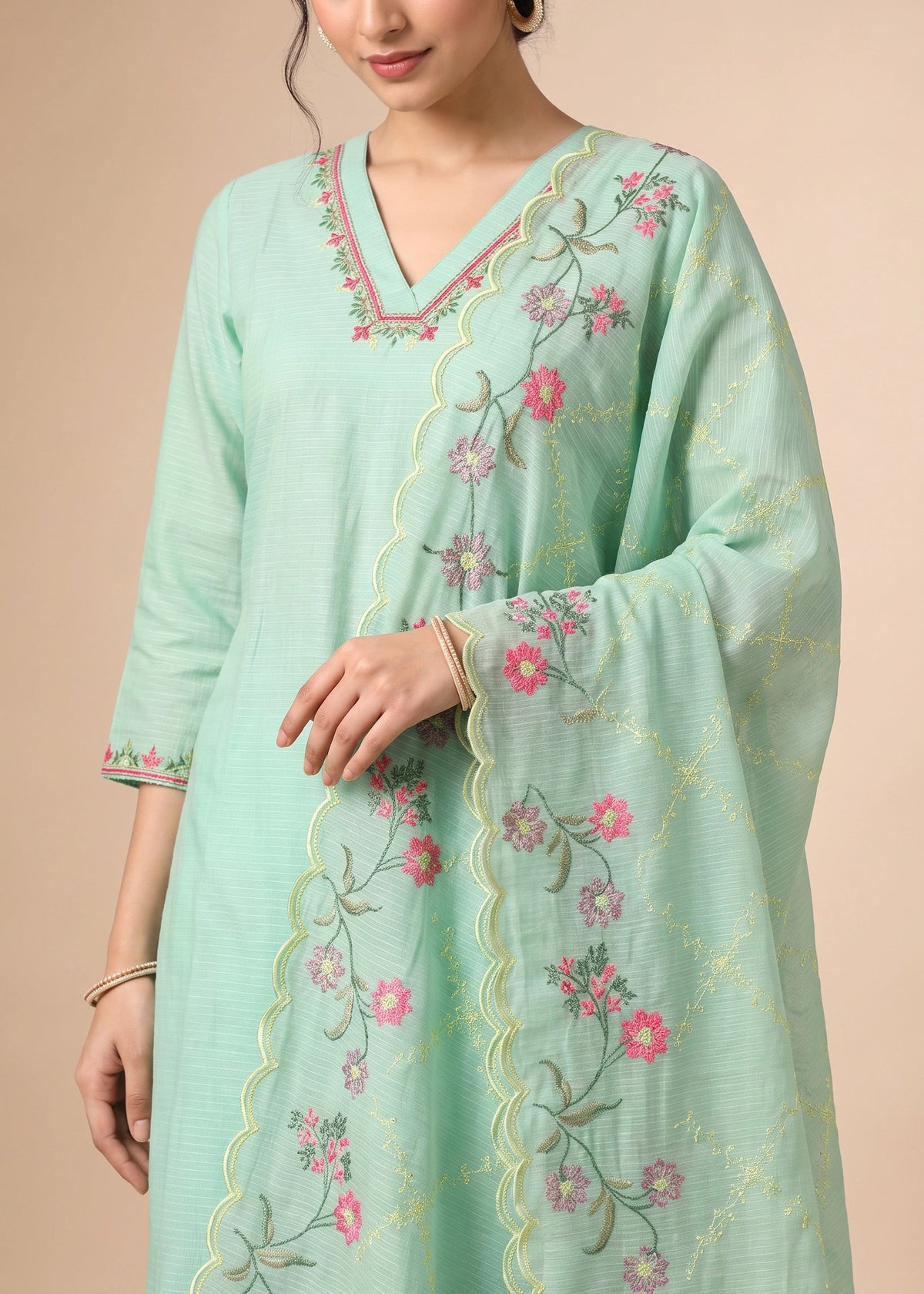 A woman wearing a mint green traditional kurta with pink floral embroidery and a matching embroidered dupatta, set against a solid beige background.