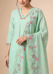 A woman wearing a mint green traditional kurta with pink floral embroidery and a matching embroidered dupatta, set against a solid beige background.