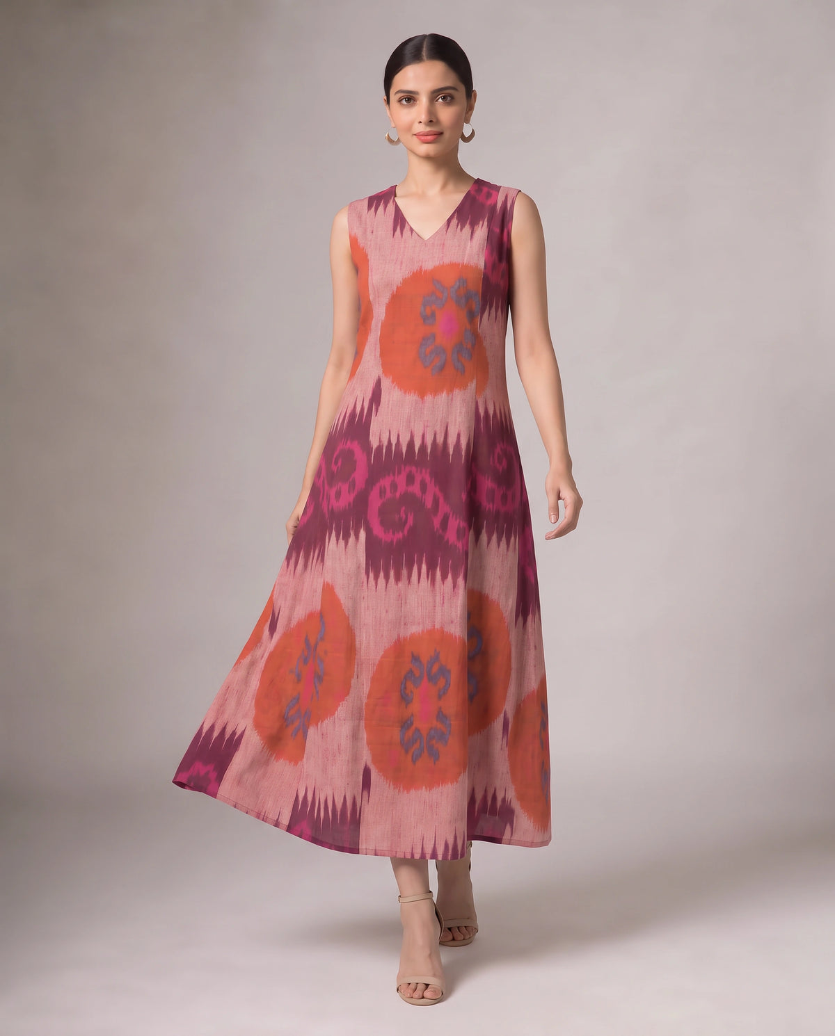 A sleeveless V-neck midi dress with a pink, orange, and purple ikat pattern, modeled against a neutral studio background.