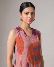 A woman modeling a sleeveless V-neck top with a pink, orange, and purple ikat pattern against a neutral gray studio background.