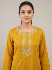 A woman wearing a mustard yellow long-sleeve kurta with intricate silver floral embroidery around the neckline, photographed against a solid light gray background.