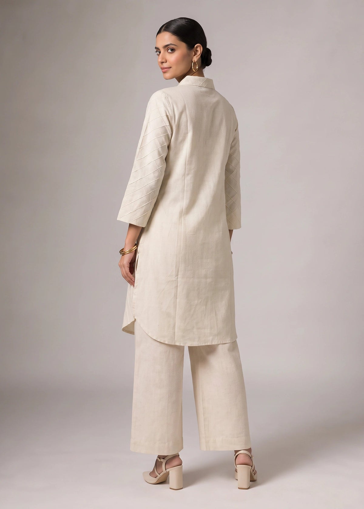 A woman modeling a light beige kurta and matching wide-leg trousers set, shown from the back against a neutral gray studio background.