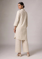 A woman modeling a light beige kurta and matching wide-leg trousers set, shown from the back against a neutral gray studio background.