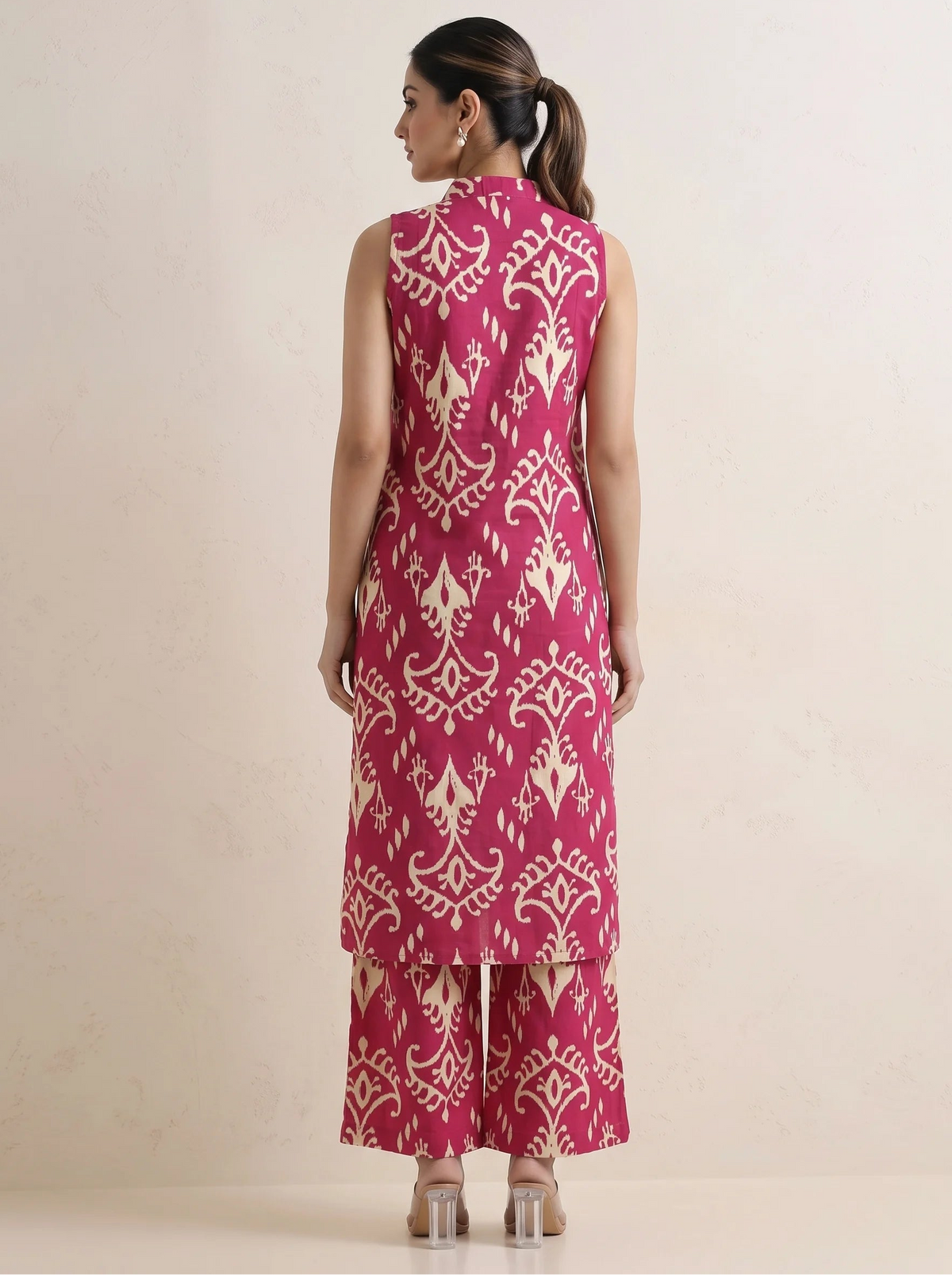 A woman shown from the back wearing a sleeveless magenta kurta and matching wide-leg pants with a cream ikat pattern, set against a plain beige studio background.