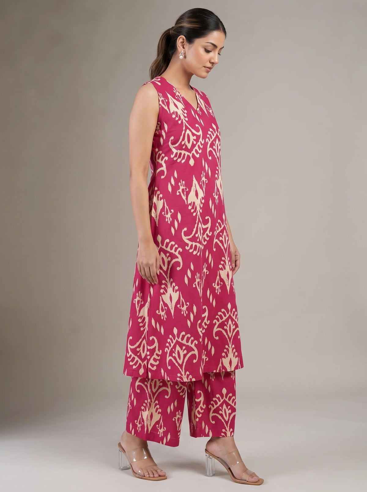 A woman modeling a sleeveless magenta pink and beige printed kurta set with matching wide-leg pants, standing against a neutral beige studio background.